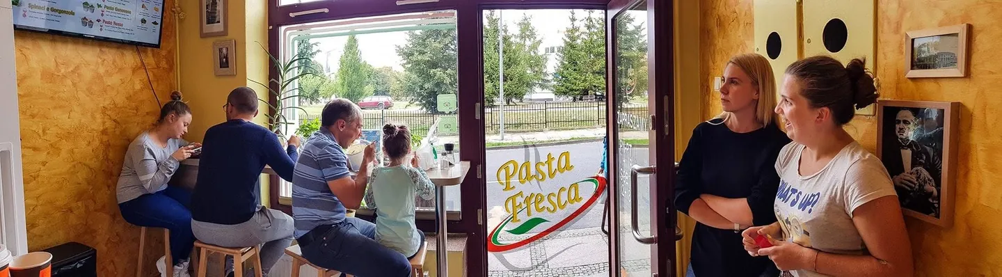 Wnętrze Pasta Fresca w centrum Szczecina: goście przy oknie i przy ladzie z otwartą kuchnią